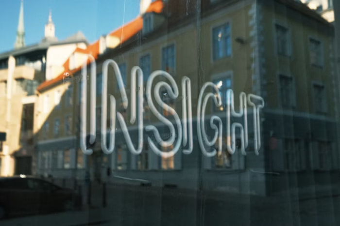 Neon sign reading “INSIGHT” reflected in a window with blurred buildings in the background.